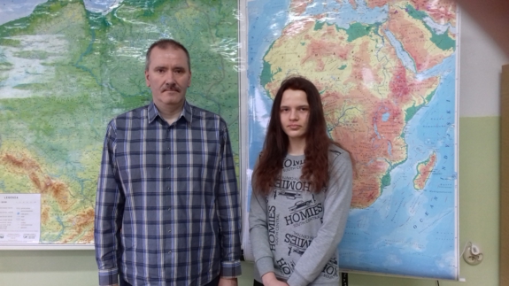 Anna Cichoń wraz ze swoim nauczcielem stojąca na tle map geograficznych