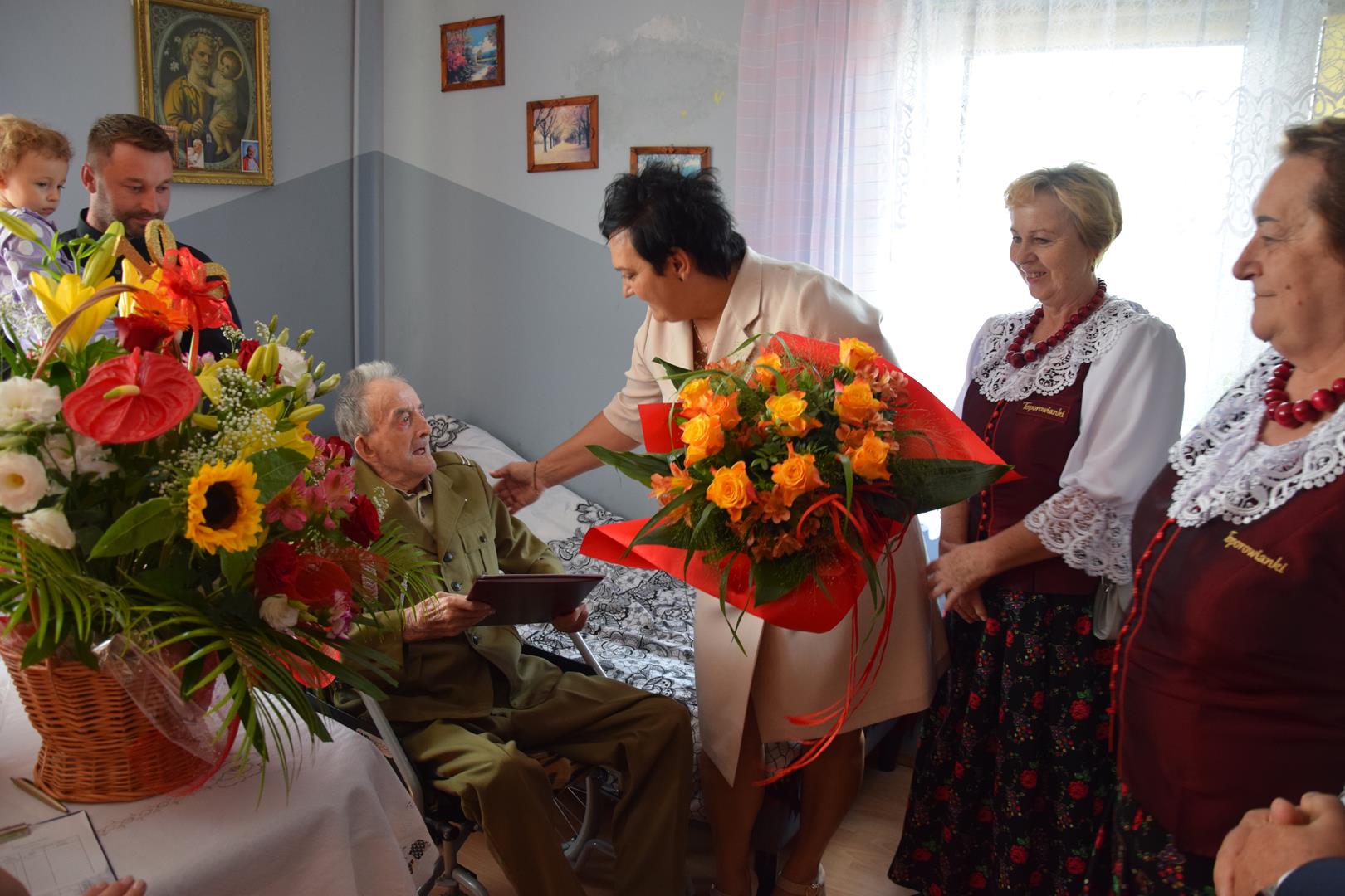 Zdjęcie przedstawiające Panią Sołtys Annę Kolasińską oraz delegację KGW Toporowice składających życzenia i kwiaty Panu Stanisławowi Piekarskiemu