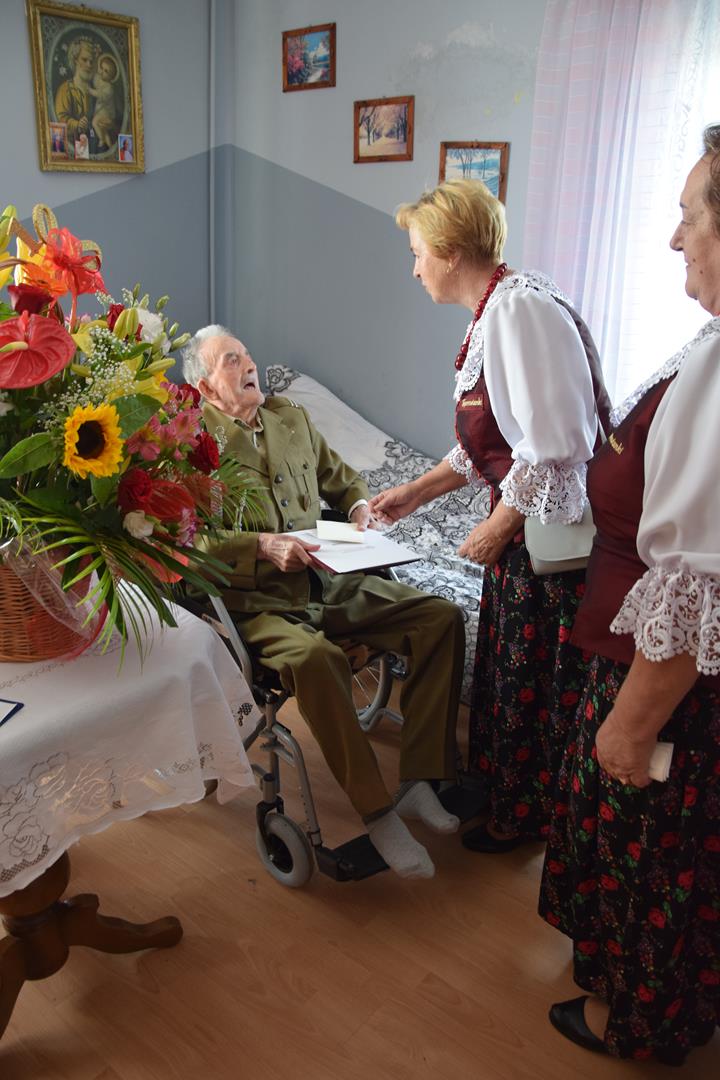 Zdjęcie przedstawiające przewodniczącą KGW Toporowice Annę Kyrcz  składającą życzenia i kwiaty Panu Stanisławowi Piekarskiemu