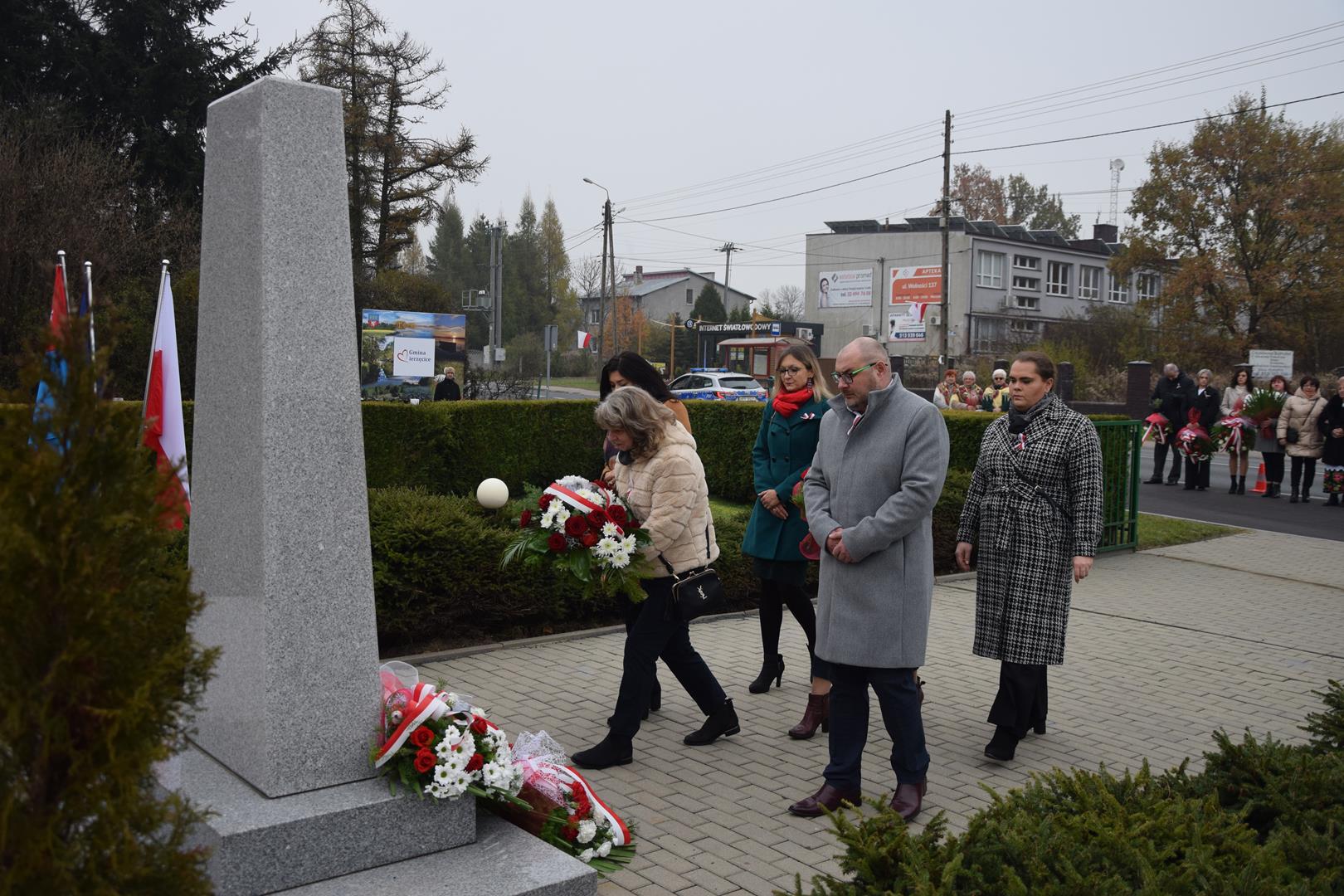 Zdjęcie przedstawia moment wręczenia kwiatów pod pomnikiem