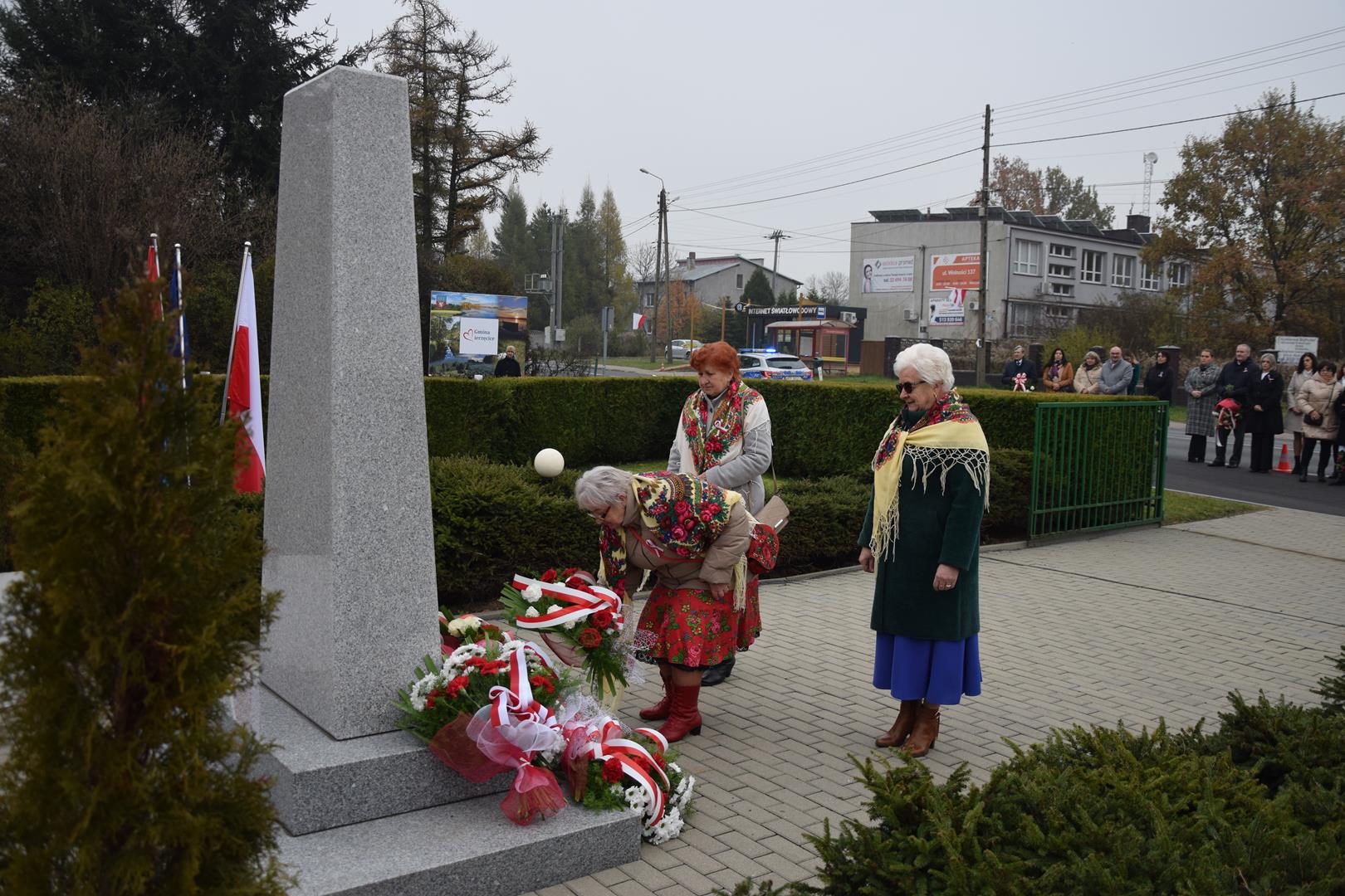 Zdjęcie przedstawia moment wręczenia kwiatów pod pomnikiem