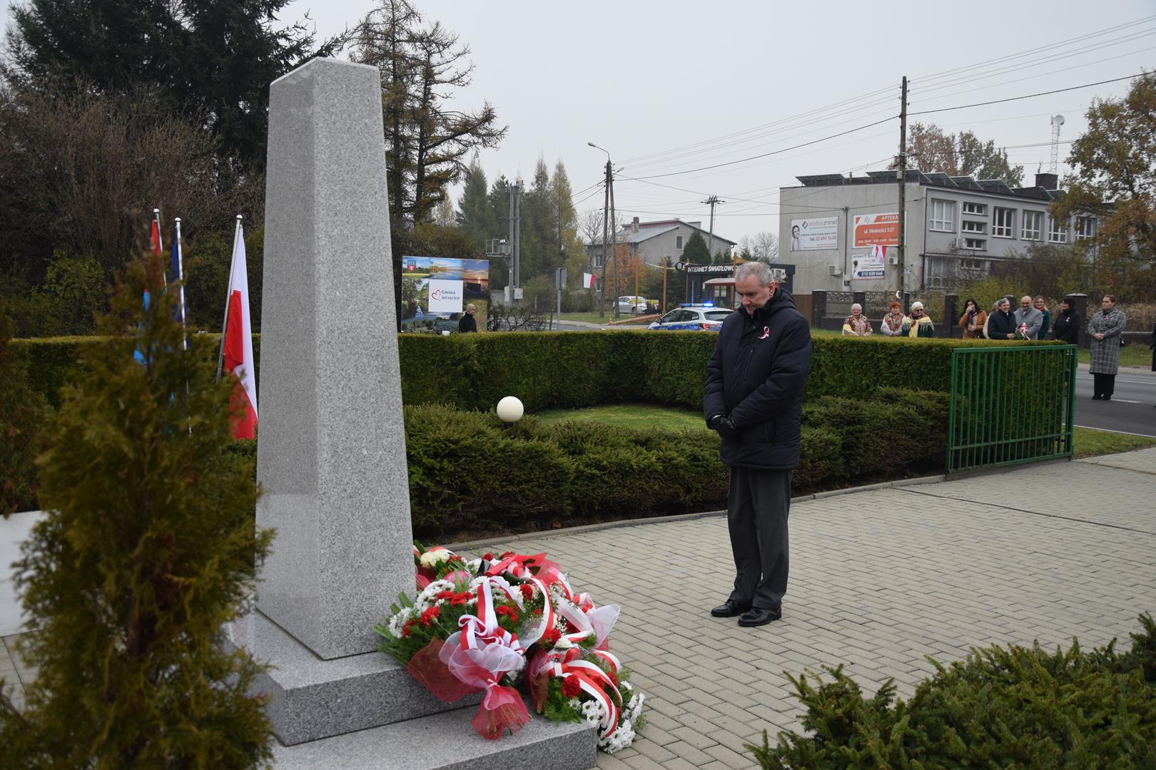 Zdjęcie przedstawia moment wręczenia kwiatów pod pomnikiem