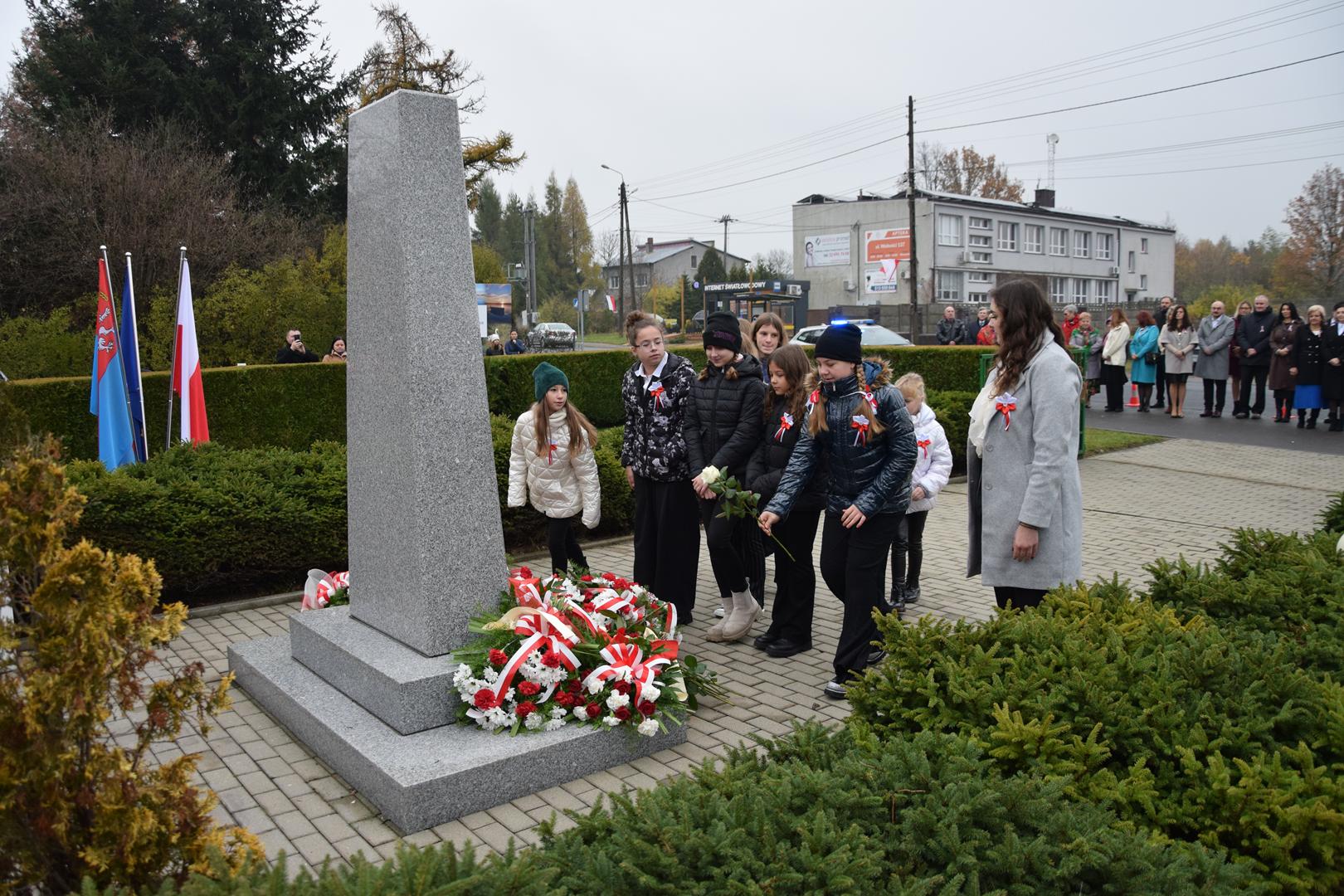 Zdjęcie przedstawia moment składania kwiatów pod pomnikiem