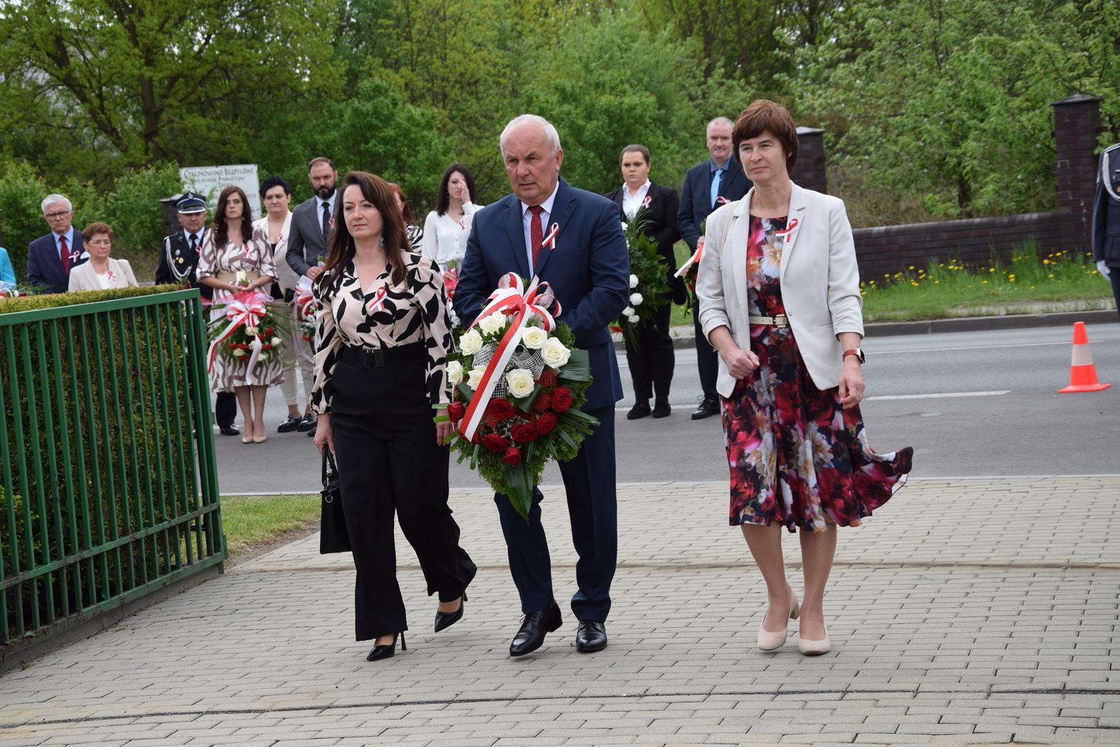 Zdjęcie przedstawia moment składania kwiatów pod pomnikiem przez Wójta Gminy Mierzęcice Grzeogrza Podlejskiego wraz z Wicewójt Iwoną Pańtą i Sekretarz Gminy Mierzęcice Iwoną Sinderą