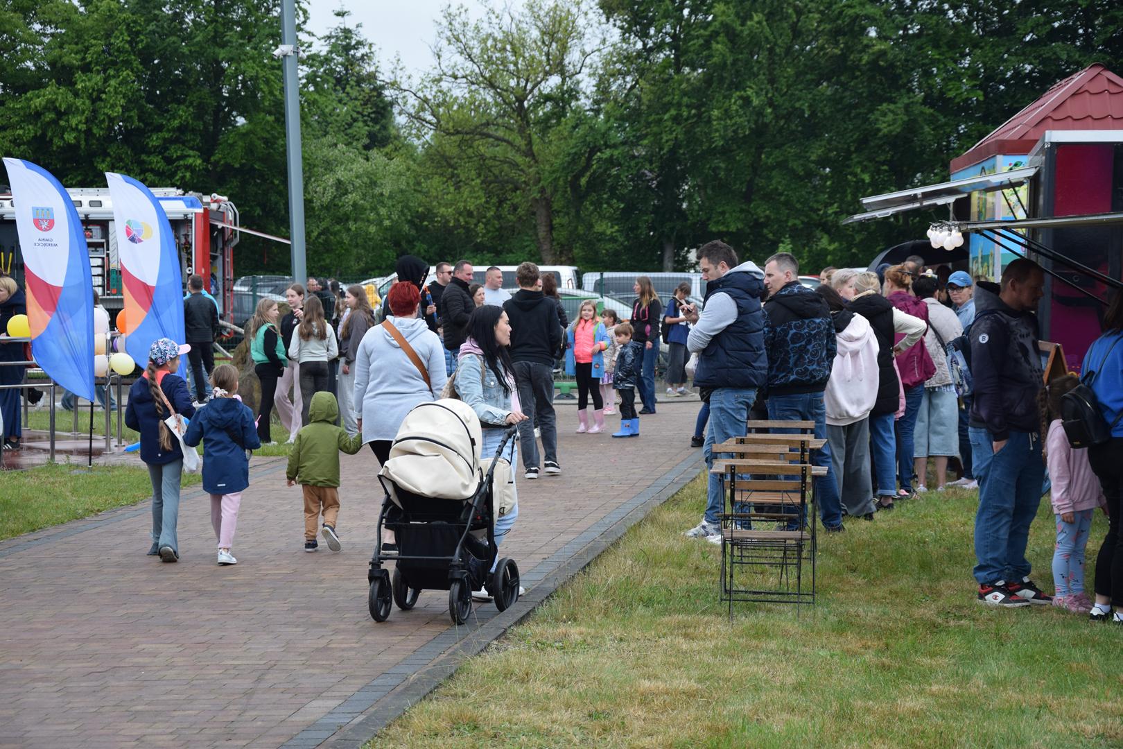 Zdjęcie przedstawia ludzi przechadzających się po terenie pikniku z okazji Dnia Dziecka