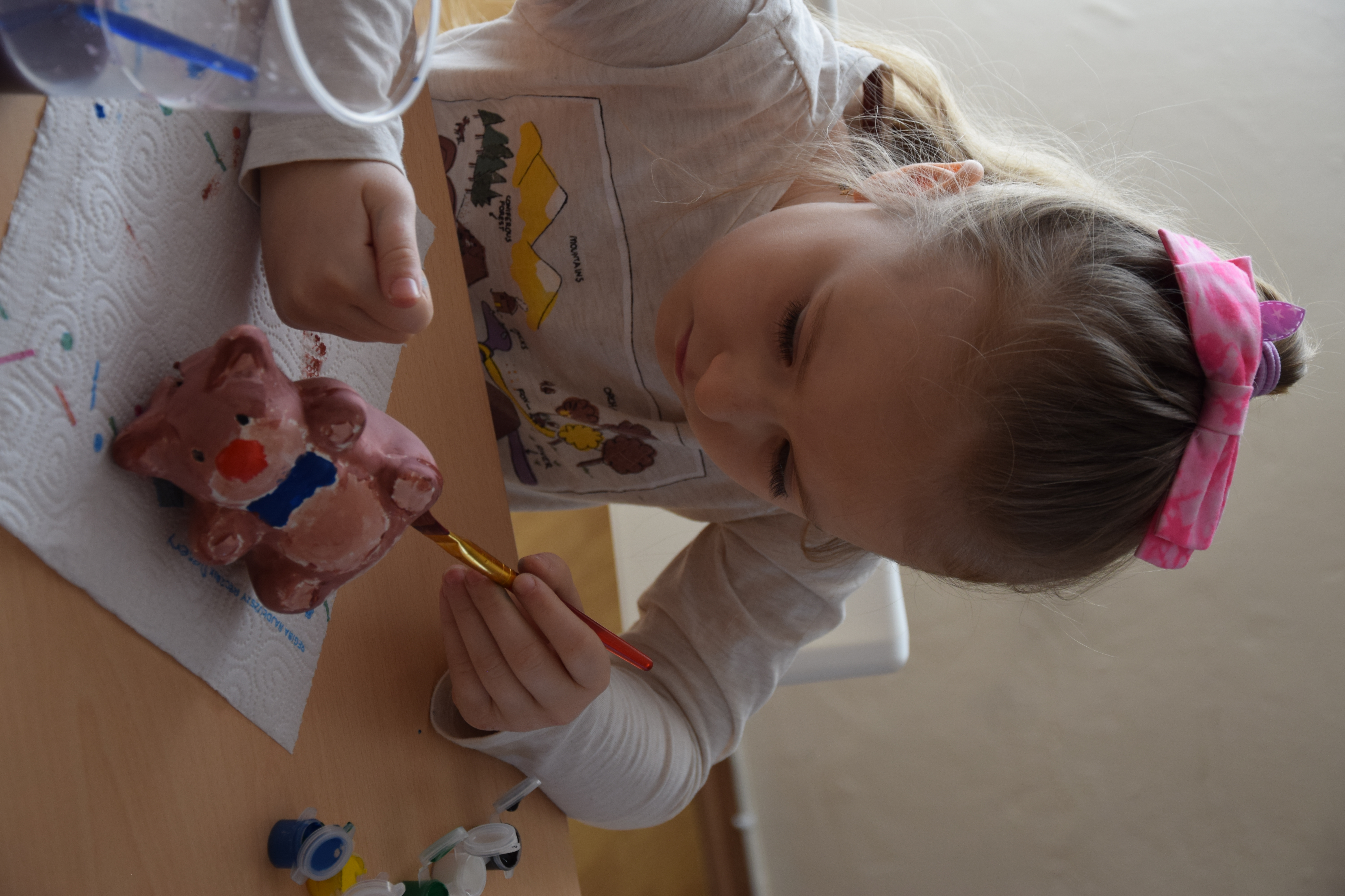 Zdjęcie przedstawiające dziecko malujące misiową skarbonkę