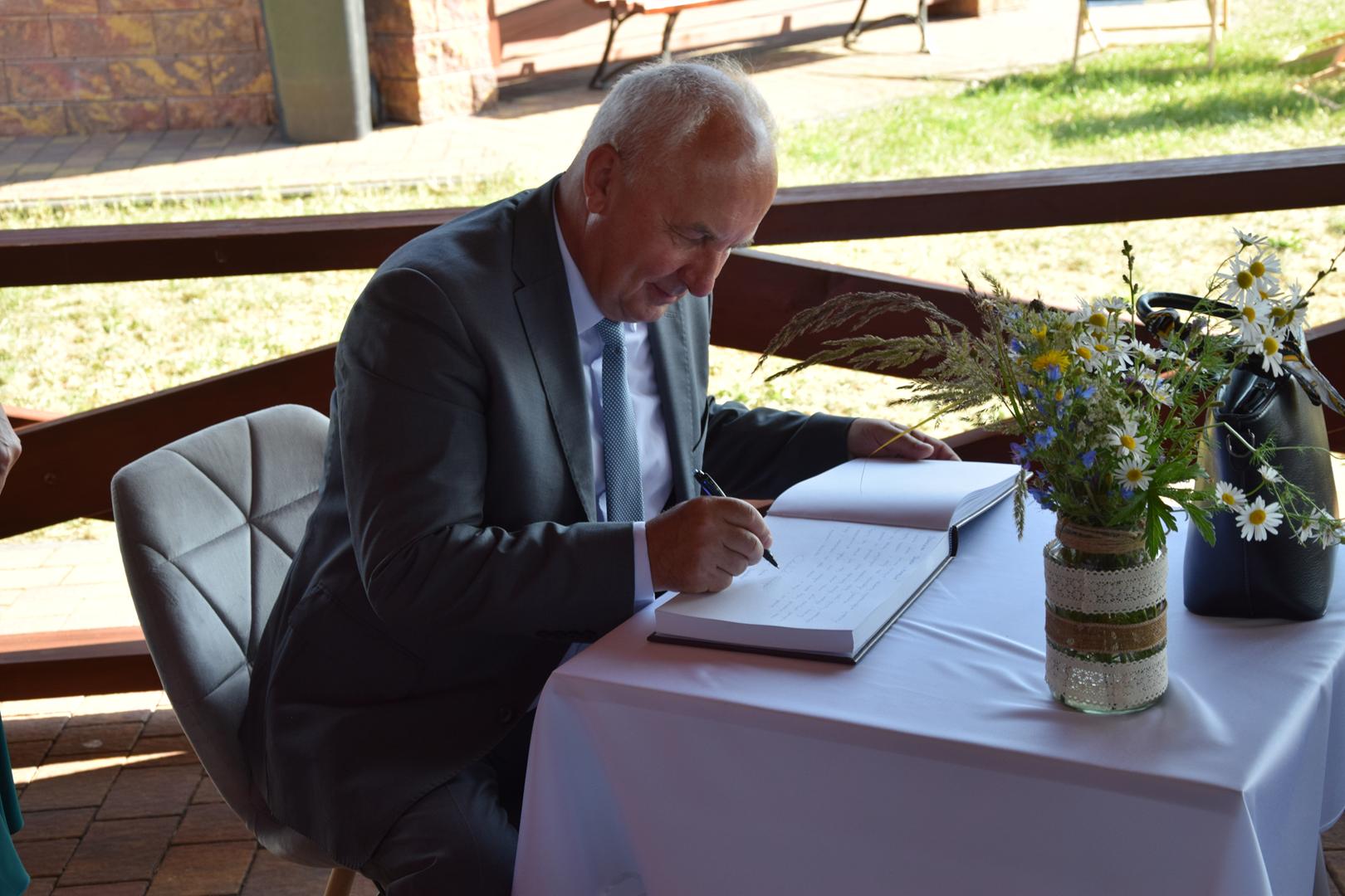 Zdjęcie przedstawia Wójta Gminy Mierzęcice Grzegorza Podlejskiego dokonującego wpisu do księgi pamiątkowej
