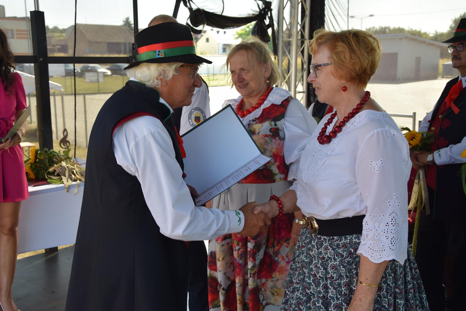 Zdjęcie przedstawia moment wręczania pamiątkowych dyplomów i&nbsp;nagród dla gości zaproszonych na Jubileusz Kapeli