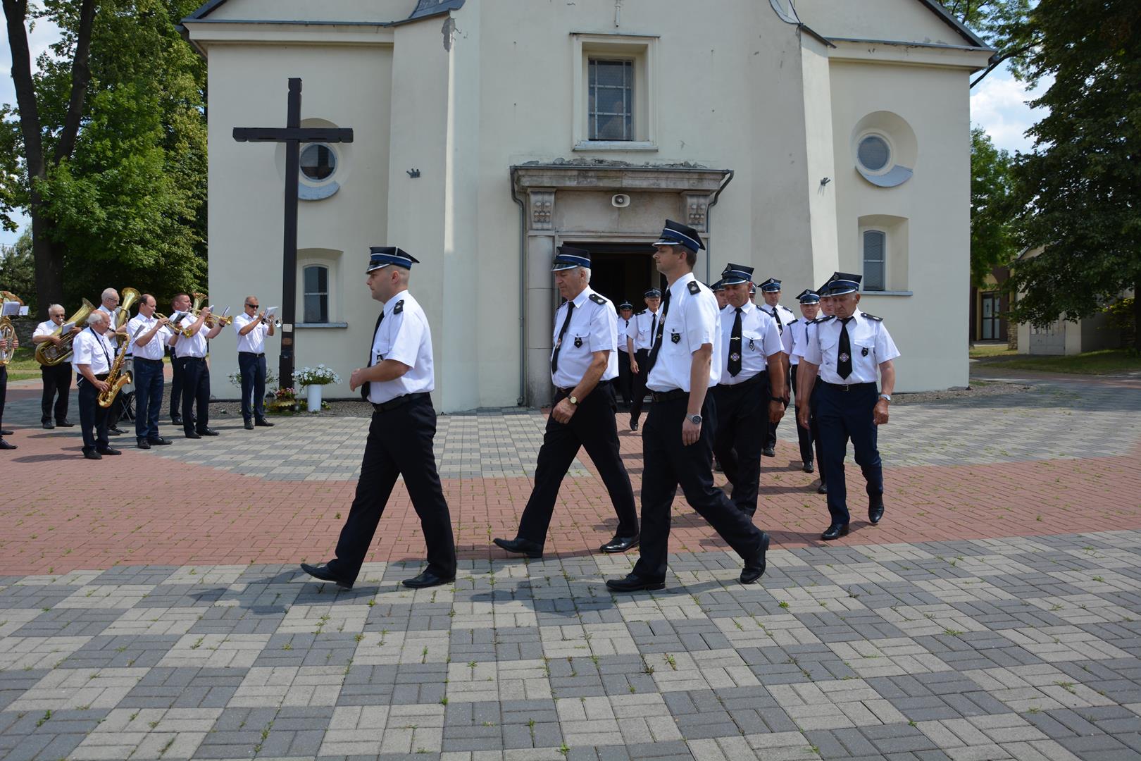 Zdjęcie przedstawiające pochód oddziału straży OSP orkiestrę grającą przed wejściem do kościoła