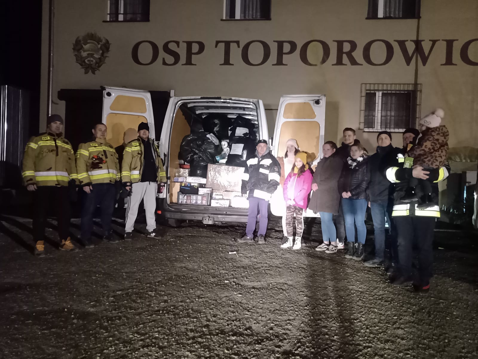 Zdjęcie przedstawiające załadowany darami samochód OSP oraz strażaków i ich przyjaciół na tle reminy OSP Toporowice