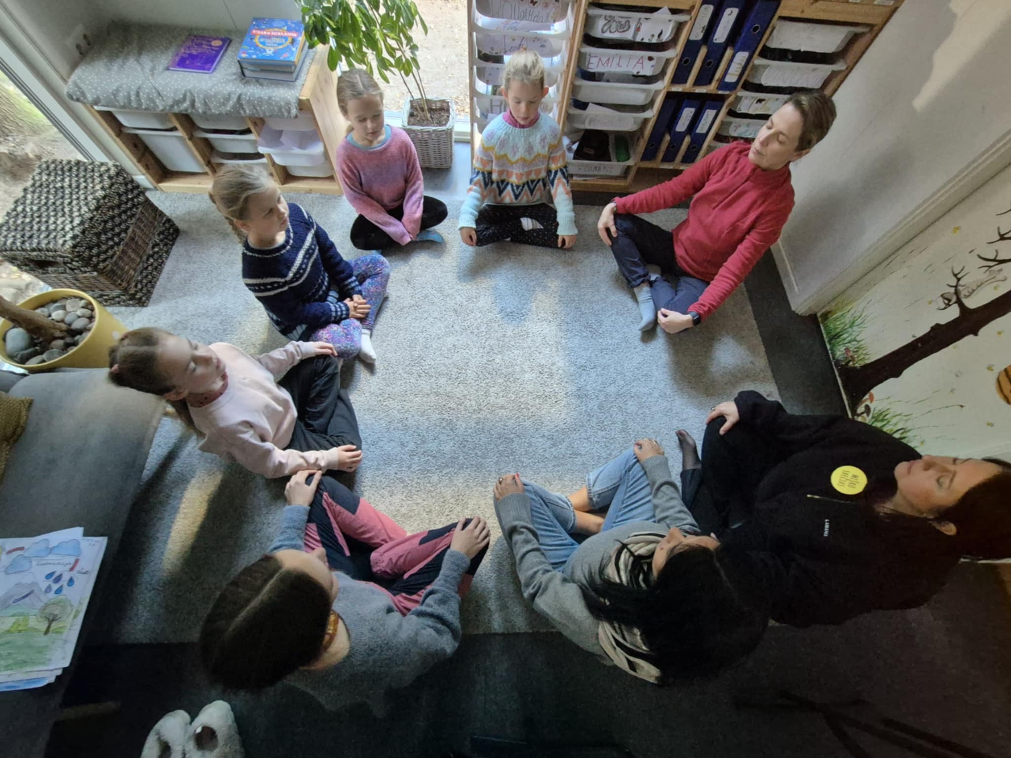 Zdjęcie przedstawia dzieci oraz dorosłych siedzących po turecku