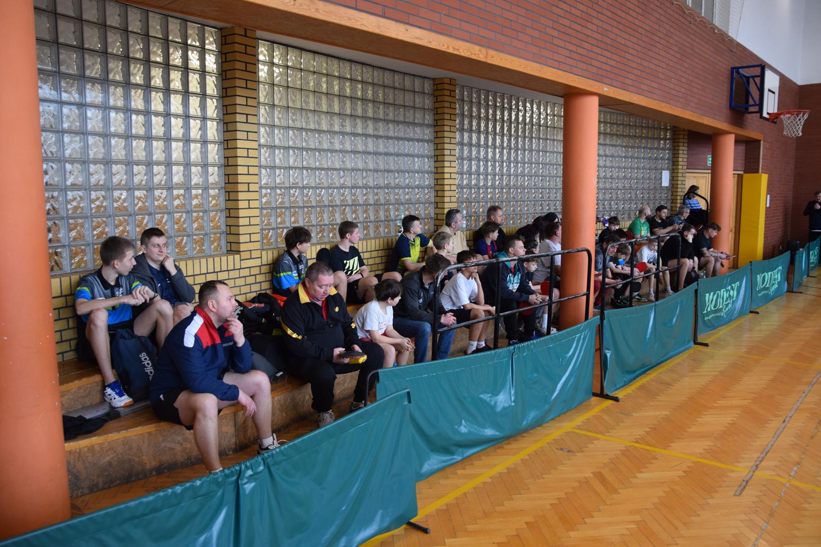 Zdjęcie przedstawia publiczość zawodów oraz zawodników siedzących na trybunach